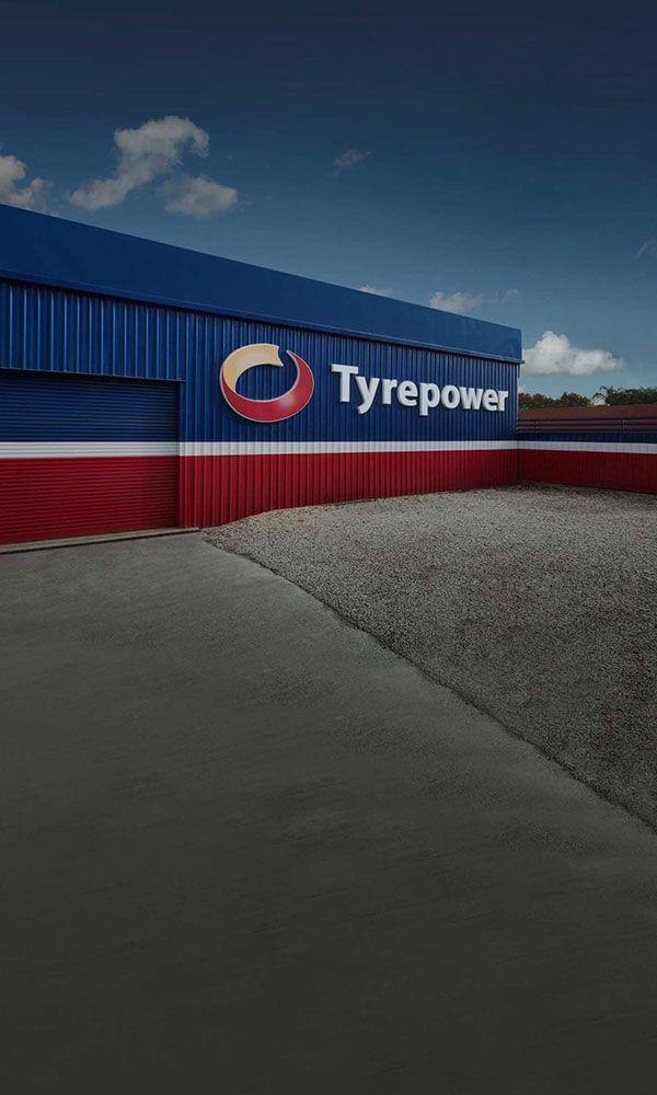 Outside of a Tyrepower store, looking at side of red, blue and white painted building.